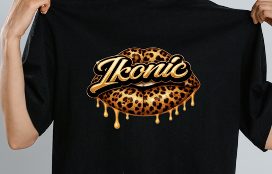 Close up of person holding a black t-shirt with 'Ikonic' logo featuring leopard print design on a plain background