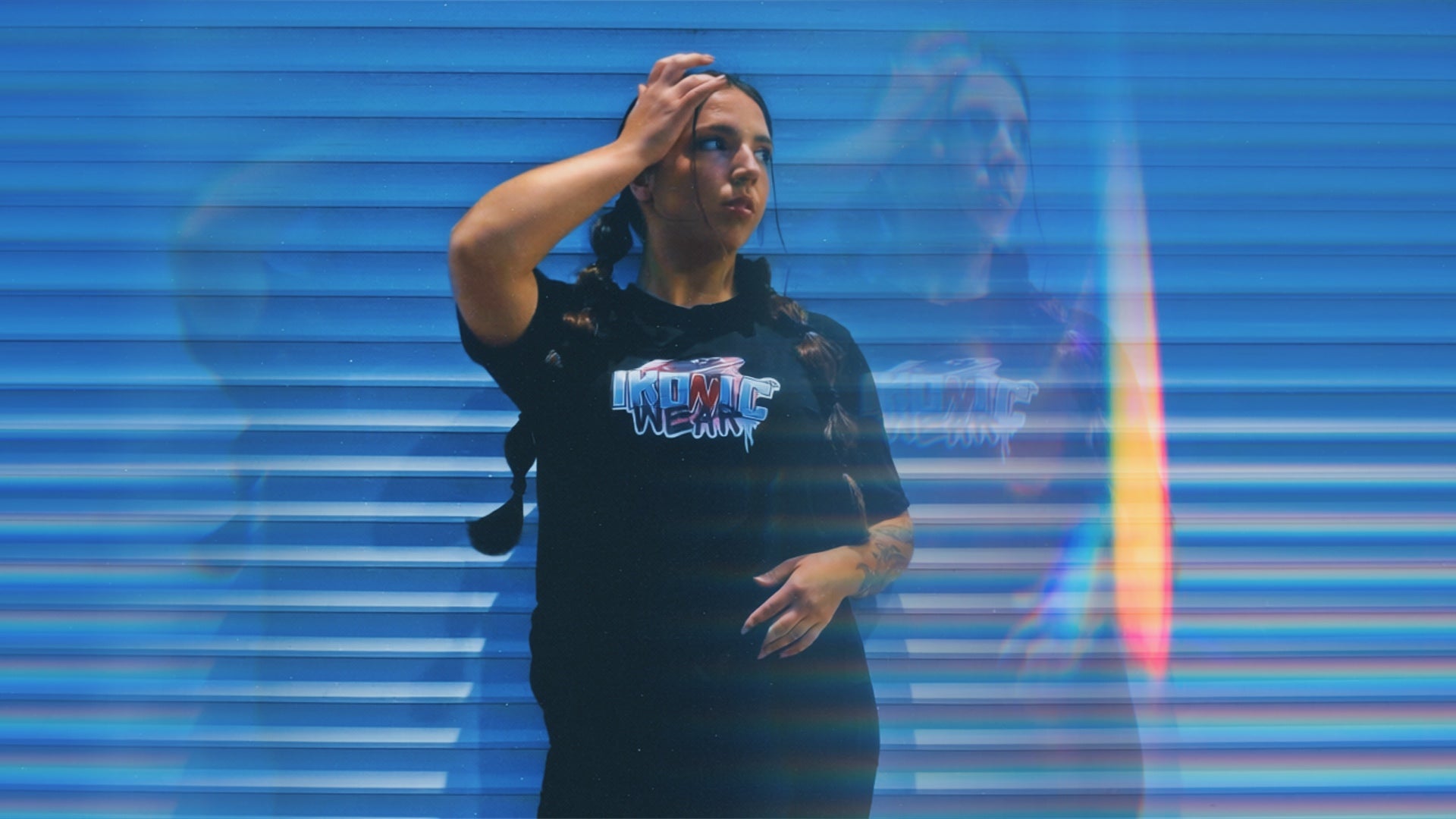 Person wearing a black t-shirt with a logo, standing in front of a reflective blue surface.