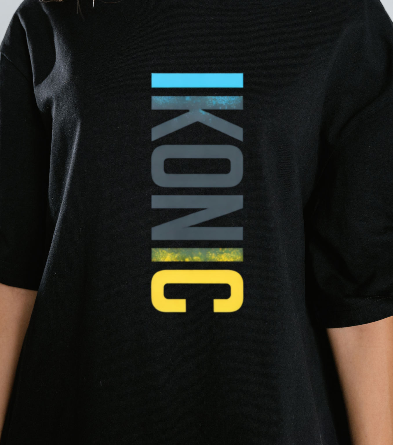 Close up of person wearing a black t-shirt with 'IKONIC' logo on a plain background