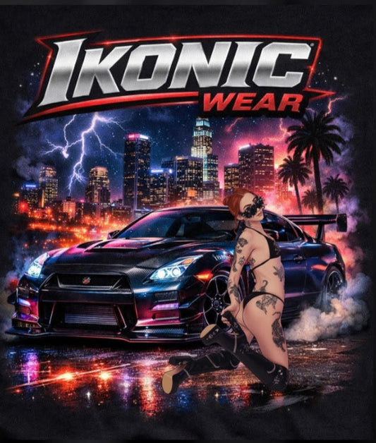 Close-up of a black t-shirt with 'Ikonic Wear' graphic design featuring a car and a person on a cityscape background.